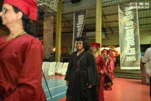 Graduates in regalia at an indoor ceremony with "Graduate Day 2025" banners.