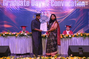 graduate receives certificate from woman, backdrop shows "Graduate Day."