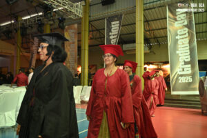 Graduates in red and black gowns at a 2025 ceremony for BBA and BCA indoors.