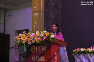 Woman at podium with flowers, speaking at BBA BCA graduation event, Regional College of Management.