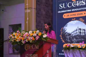 Woman speaking at podium with flowers during graduation at Regional College of Management.