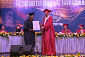 Graduate receives certificate from official on stage during a convocation event, with seated attendees.