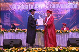 Graduate receiving certificate on decorated stage during Convocation 2025 ceremony.