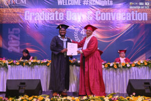 Graduate in black gown receives certificate from faculty in red robe during convocation ceremony.