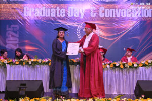 Graduation ceremony with graduate receiving certificate, backdrop reads "Graduate Day & Convocation 2025".