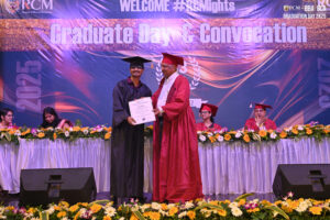 Graduate in black cap and gown receives certificate on stage; banner reads "Graduate Day & Convocation".