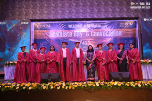 Graduates in ceremonial robes on stage at RCM convocation event with floral decorations.