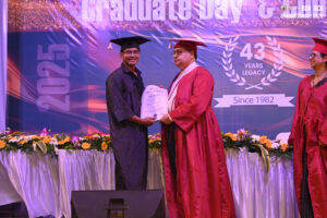 Graduate receiving certificate on stage, 43rd institution anniversary, 2025 banner background.