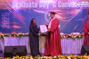 Graduate receives certificate on stage with 2025 convocation banner in background.