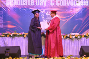 Graduate receives certificate from person in red robe at decorated convocation ceremony stage.