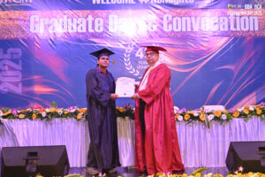 Graduate receiving certificate from official in red gown at convocation ceremony.