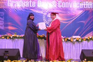 Graduation ceremony with a certificate presentation, decorated stage, and "Graduate Day" banner.