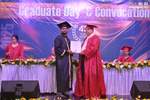 Graduation ceremony with certificate presentation, academic regalia, and decorative background.