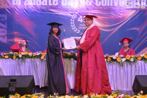 Graduate receives certificate from officiant on stage with floral decor at convocation ceremony.