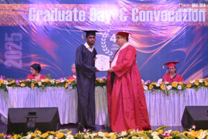 Graduate in cap and gown receives certificate from official on stage at 2025 convocation.