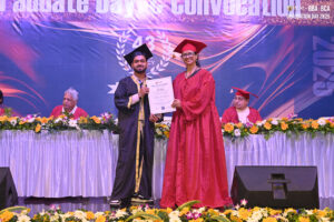 student receives certificate on stage, banner reads "Graduate Day Convocation."