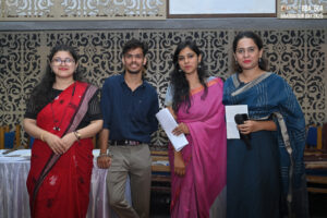Four graduates at an event, three women in sarees and a man in a dark shirt, with decor.
