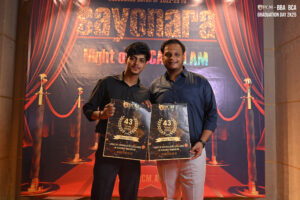 Two people at "Graduation Day 2K25" holding posters about 43 years of RCM's legacy.