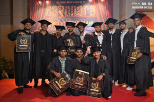 Graduates in black caps and gowns on stage holding certificates, with a graduation backdrop.