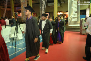 Graduates in caps and gowns process indoors near banners and arranged chairs.