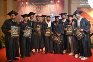 Graduates in black caps and gowns on a red carpet holding certificates at a ceremony.