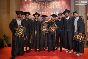 Eight graduates in black gowns and caps on red carpet, holding certificates, with festive backdrop.