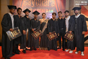Graduates in caps and gowns with certificates pose with a woman in saree on Graduation Day.