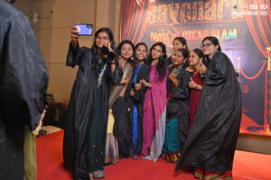 Group taking a selfie at "Night of Oscar Glam" graduation event, wearing gowns.