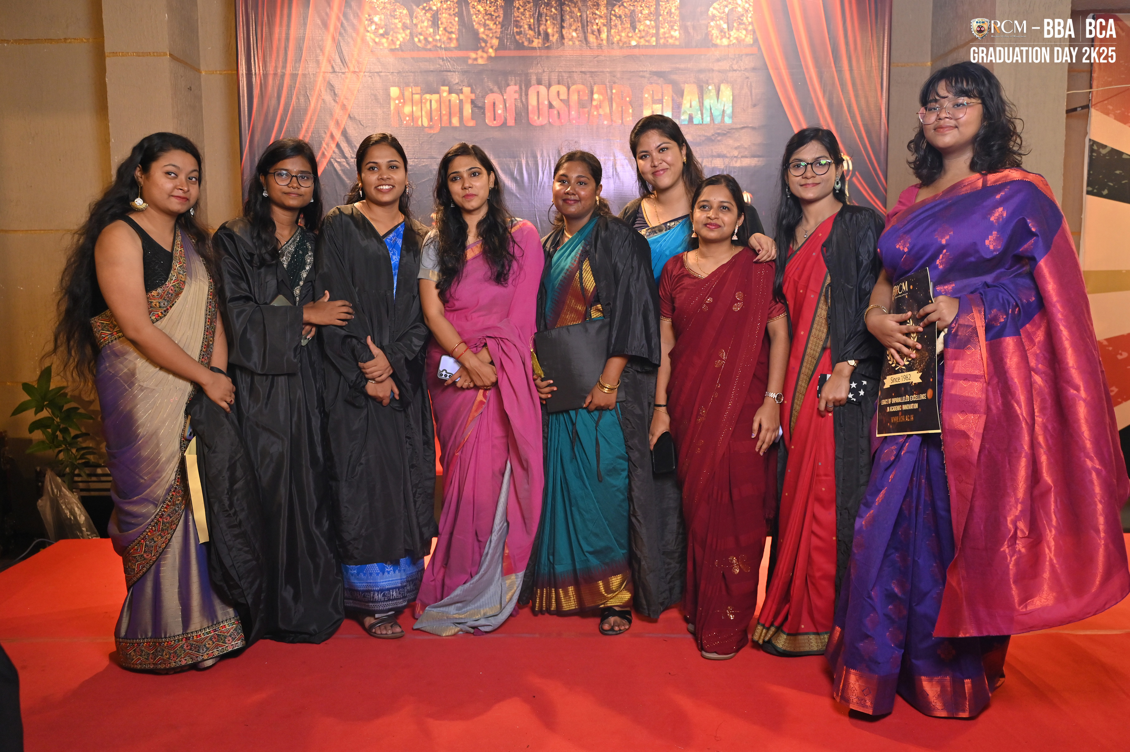 People in traditional attire and gowns on red carpet at "Oscar Glam" themed graduation event.