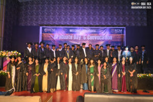 Graduates in caps and gowns pose on stage at RCM Global School's BBA BCA convocation ceremony.