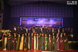 Graduates posing in caps and gowns at RCM Global School convocation with event banners.