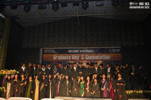 Graduates in black gowns on stage during RCM Global B-School convocation ceremony.