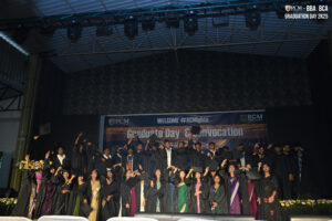 Graduates in black gowns celebrate on stage at RCM Global School's convocation for BBA and BCA.