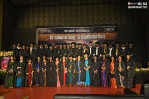 Graduates in caps and gowns pose on stage with "Graduate Day & Convocation" sign.