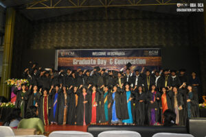 Graduates in black gowns on stage with "Graduate Day & Convocation" banner at RCM Global School.