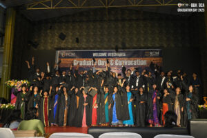 Graduates in caps and gowns celebrating on stage, tossing caps, with a "Graduation Day" banner.
