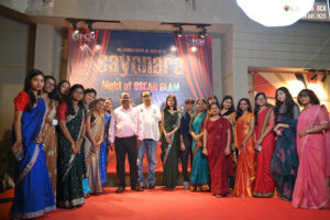 Group of people at an indoor event with a "Night of Oscar Glam" banner.