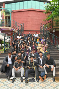 Graduates in gowns and casual wear on steps of brick building, "Graduation Day 2K25" banner.