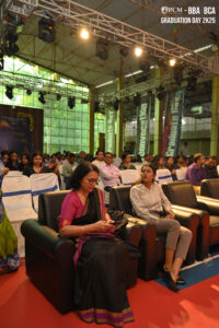 Indoor graduation event with seated attendees under bright stage lights and decorated banners.
