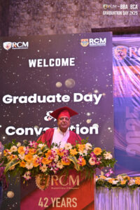 Individual in red graduation outfit at podium, "Graduate Day & Convocation" RCM backdrop.