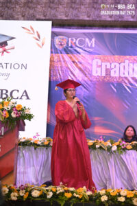 Person in red gown speaking at RCM's Graduation Day 2025 for BBA/BCA programs.