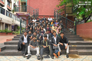 Group of graduates in formal attire on outdoor stairs with brick building backdrop.