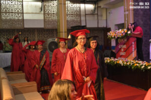 People in caps and gowns at a graduation ceremony on a red carpet, with flowers and podium.
