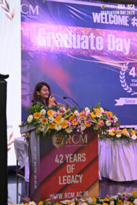 Woman speaking at podium with flowers at Regional College of Management 2025 graduation event.