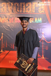 A graduate in cap and gown holds a certificate against a celebratory backdrop.