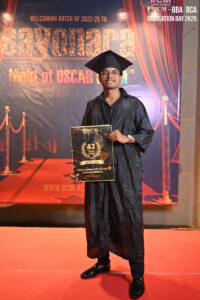 Person in graduation attire holding a plaque on a red carpet. Banner reads "Sayonara Night of Oscar."