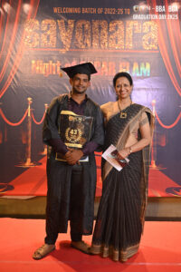 Graduation ceremony with a graduate holding certificate, standing by a woman in traditional dress.