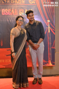 Two people posing at RCM's Graduation Day 2K25, dressed formally, with a themed backdrop.