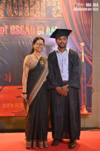 Graduate in cap and gown with woman in saree on red carpet, Graduation Day 2K25 backdrop.