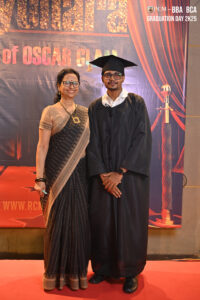 Woman in sari and man in graduation gown on red carpet at 2025 BBA/BCA event backdrop.
